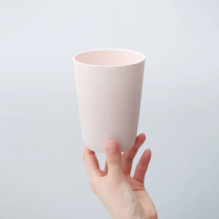 手で持つシンプルな淡いピンクのカップ